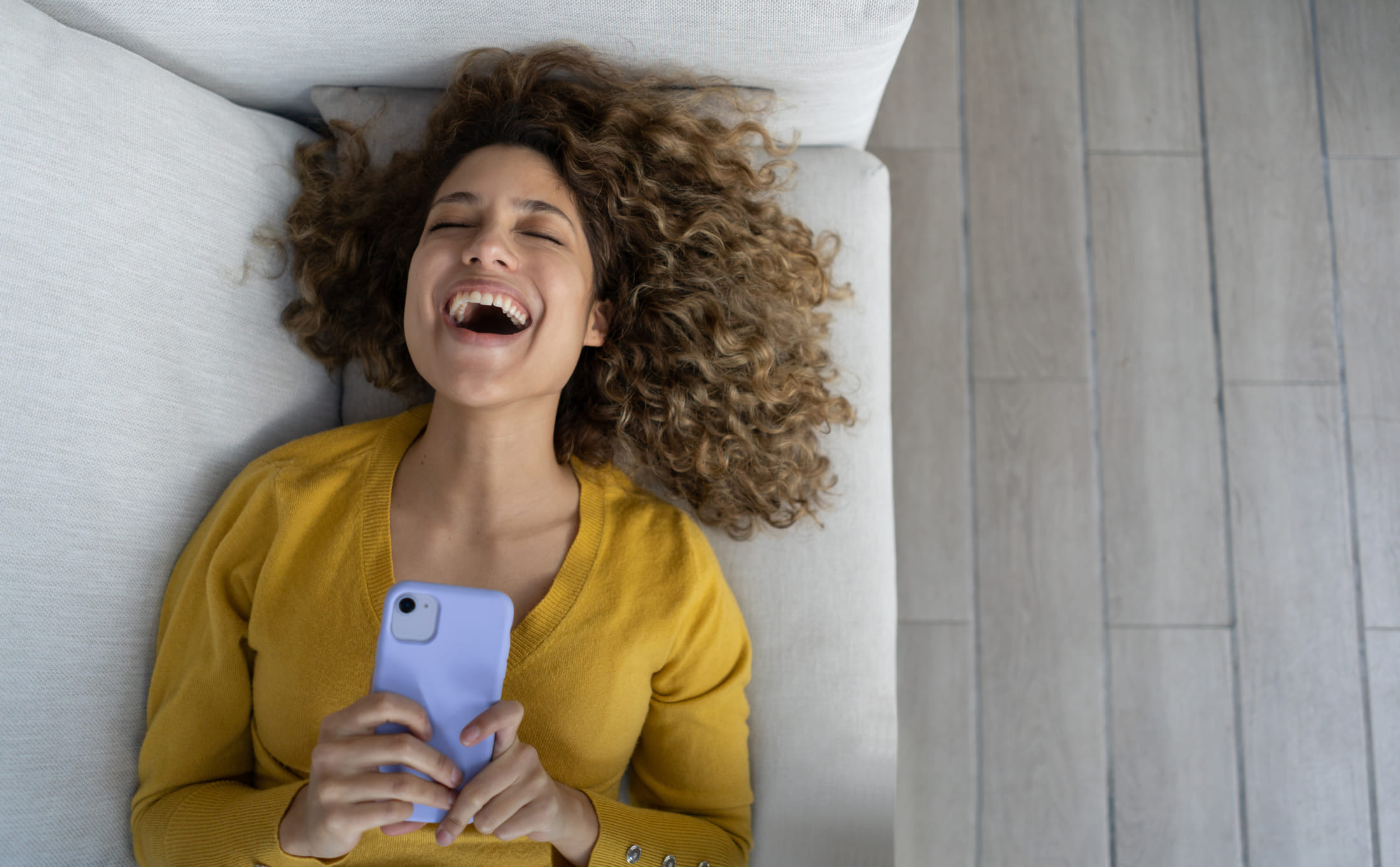 Woman laughing while looking at her smartphone, representing the study of how funny pandemic memes can help reduce COVID-related stress
